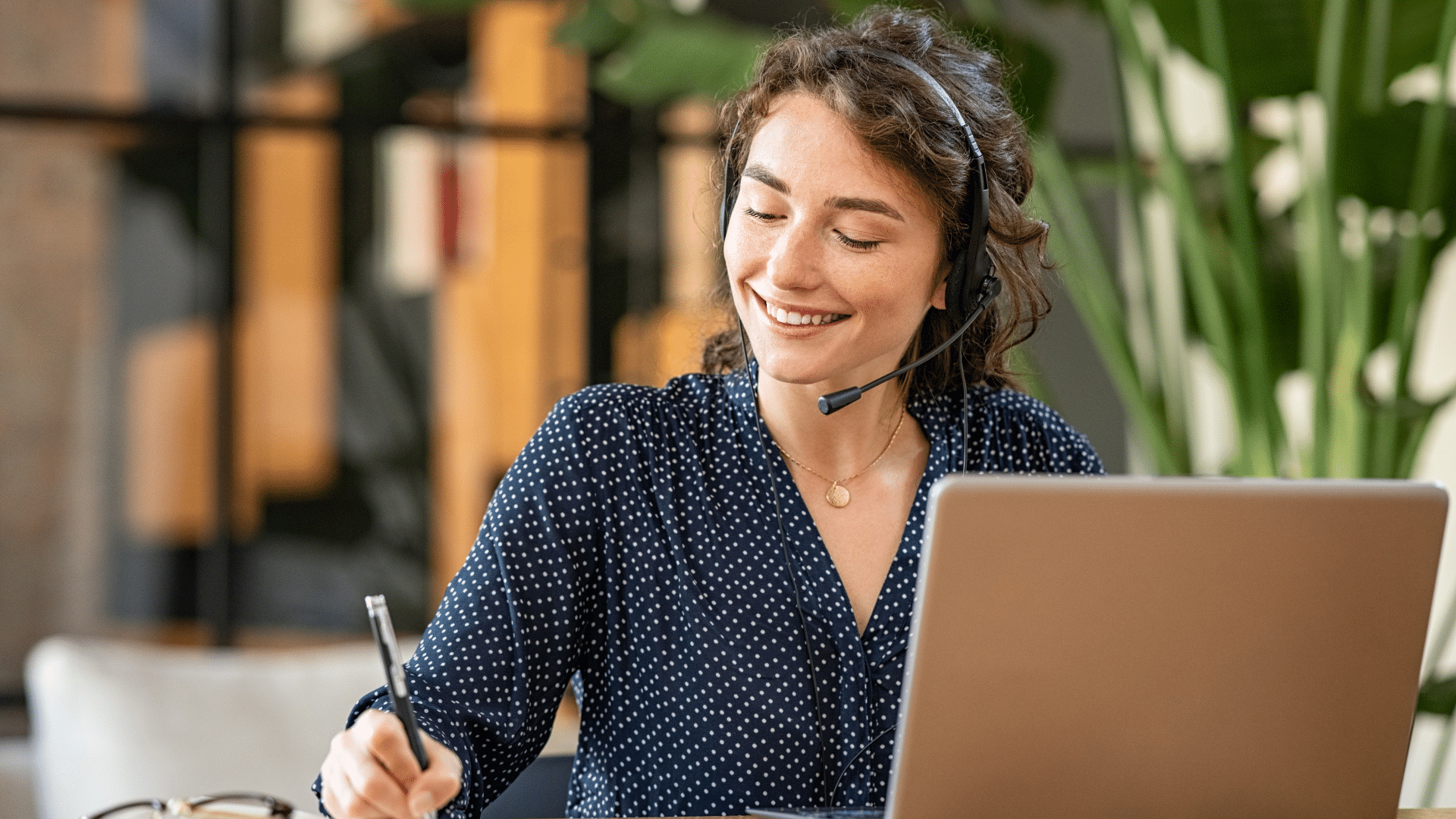 Vrouw met headset en pen in hand achter laptop