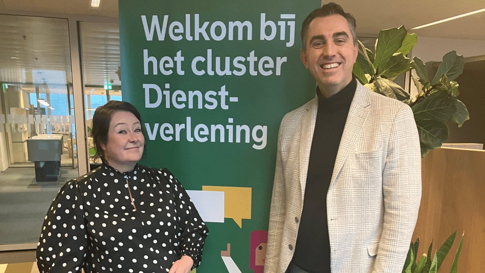 Evelien Klomps (links) en Danny Colijn bij bord met tekst ‘Welkom bij het cluster Dienstverlening’