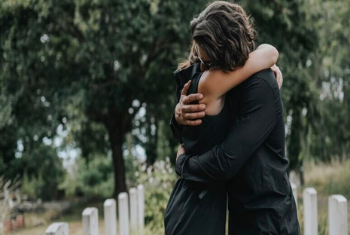 Twee mensen omhelzen elkaar op een begraafplaats